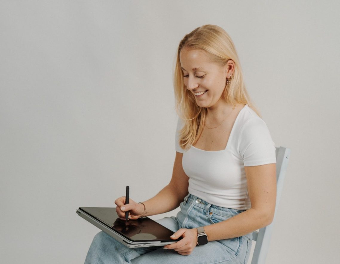 Willkommens-Bild von VIANDA Blonde Frau sitzt lächelnd und arbeitet mit einem Grafiktablett.