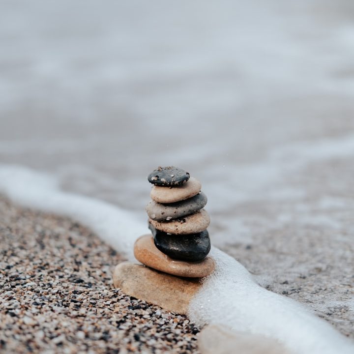 Bild zur mentalen Stabilität Steinhaufen am Strand, umgeben von sanften Wellen und feinem Sand.