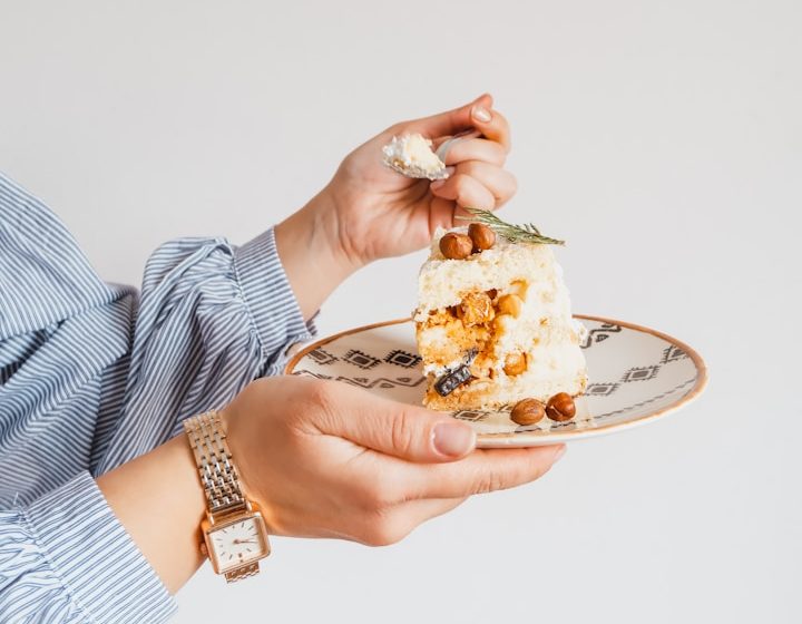 Titelbild zum emotionalen Essen Hand mit Gabel hält ein Stück Torte auf einem dekorativen Teller.